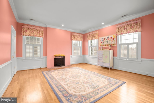 living area featuring visible vents, a fireplace with flush hearth, a wainscoted wall, wood finished floors, and crown molding