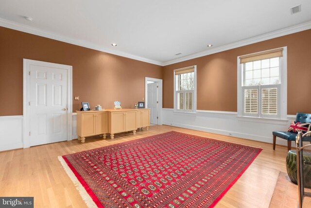 living area with wainscoting, visible vents, light wood-style flooring, and crown molding