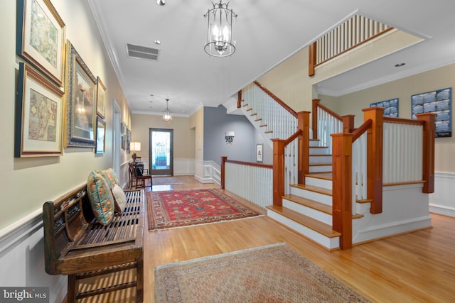 entrance foyer featuring visible vents, stairway, a wainscoted wall, ornamental molding, and wood finished floors