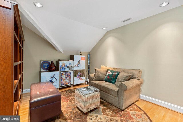 living room with visible vents, baseboards, wood finished floors, and vaulted ceiling