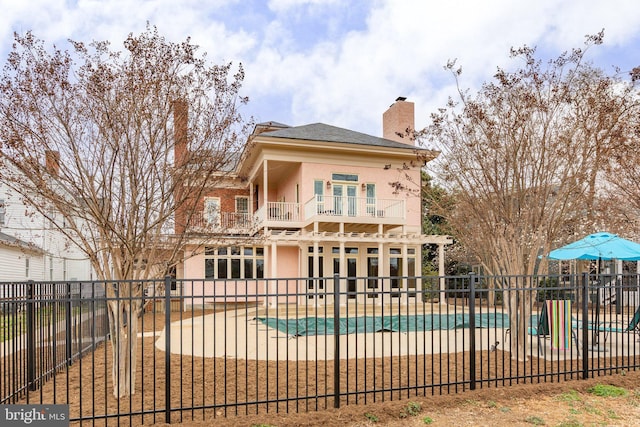 rear view of house featuring a balcony, a fenced in pool, a fenced backyard, stucco siding, and a patio area