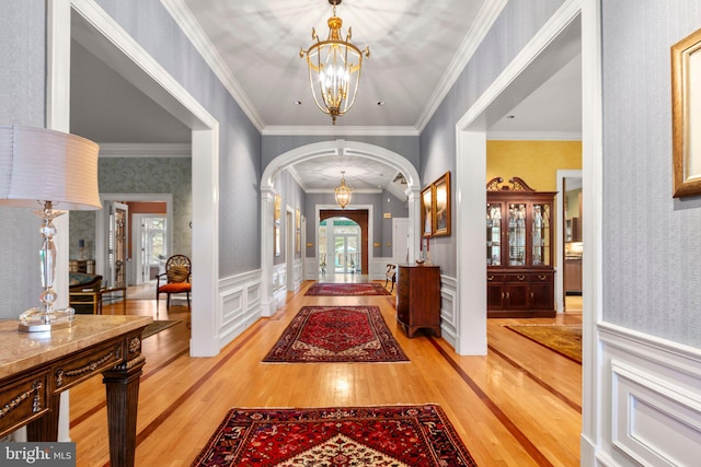 foyer featuring wallpapered walls, wainscoting, light wood-style flooring, arched walkways, and a notable chandelier