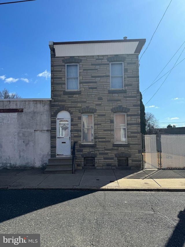 view of front of house with entry steps, stone siding, fence, and a gate