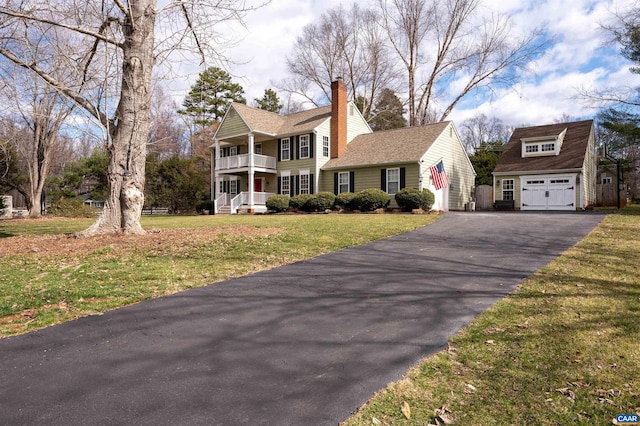 view of front of home with driveway, a balcony, a chimney, an outbuilding, and a front yard