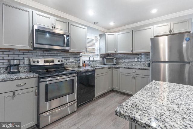 kitchen with light stone countertops, a sink, decorative backsplash, stainless steel appliances, and light wood-type flooring