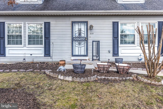 doorway to property with a lawn and roof with shingles