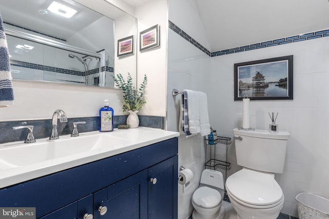 bathroom featuring a shower with door, toilet, vanity, and tile walls