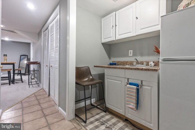 kitchen featuring light colored carpet, recessed lighting, freestanding refrigerator, white cabinets, and a sink