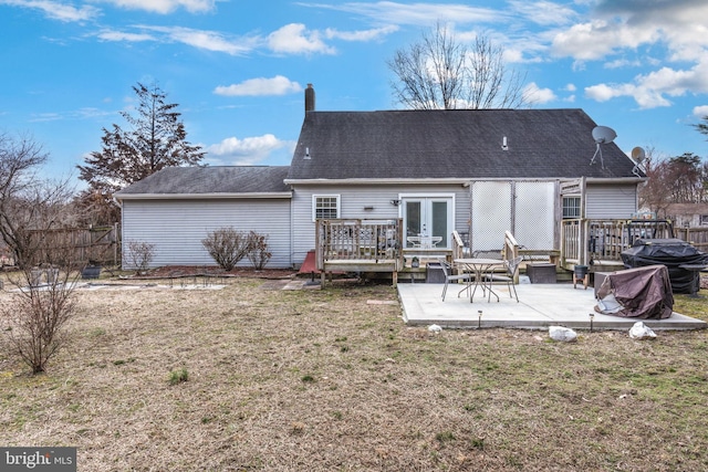 back of house with a chimney, french doors, a deck, a patio area, and a lawn