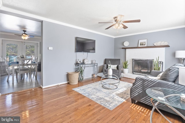 living area featuring a brick fireplace, crown molding, baseboards, ceiling fan, and wood finished floors