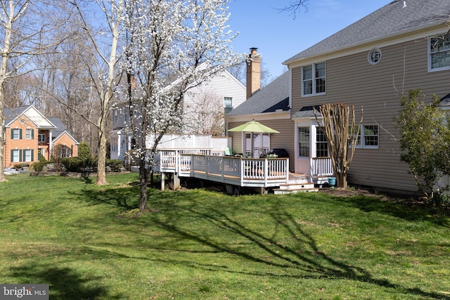 back of property featuring a yard, a chimney, and a deck