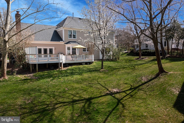 rear view of house with a yard, a deck, a chimney, and a shingled roof