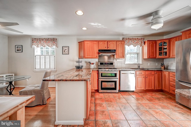 kitchen featuring a peninsula, under cabinet range hood, stainless steel appliances, and a ceiling fan