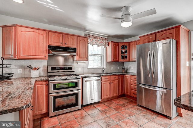 kitchen featuring stainless steel appliances, backsplash, a ceiling fan, dark stone countertops, and under cabinet range hood