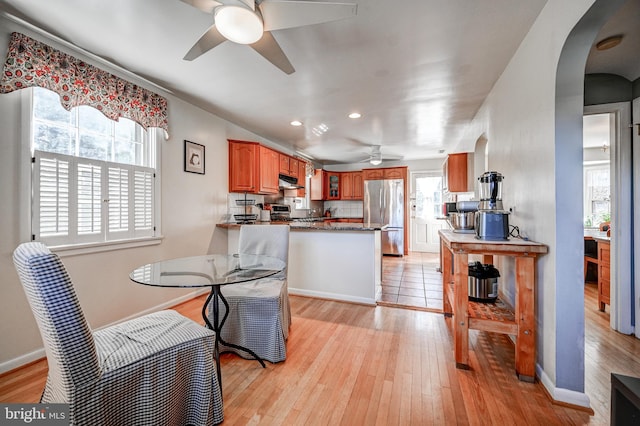 dining space featuring a ceiling fan, light wood-type flooring, plenty of natural light, and arched walkways