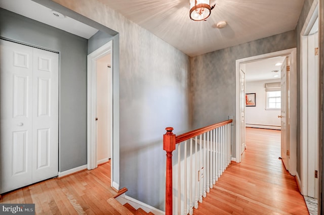 hallway featuring baseboards, a baseboard heating unit, wood finished floors, and an upstairs landing