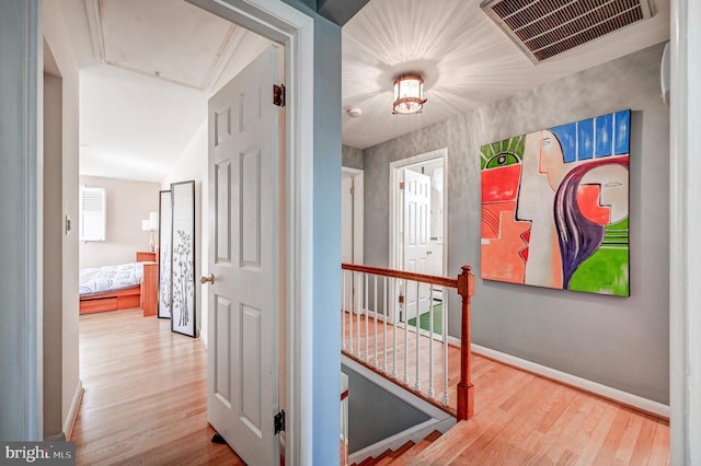 hallway featuring attic access, baseboards, visible vents, wood finished floors, and an upstairs landing