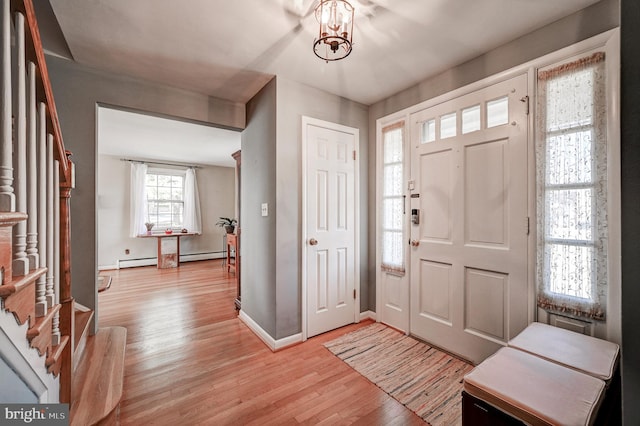 foyer entrance featuring light wood finished floors, baseboards, stairway, an inviting chandelier, and a baseboard heating unit