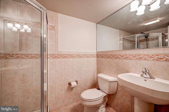 bathroom featuring tile walls, toilet, a sink, a shower stall, and a chandelier