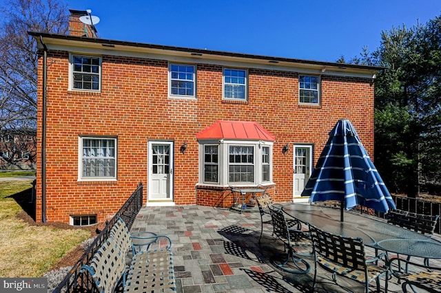 back of property featuring outdoor dining space, brick siding, a patio, and a chimney