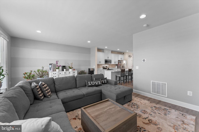 living room with recessed lighting, visible vents, light wood finished floors, and baseboards