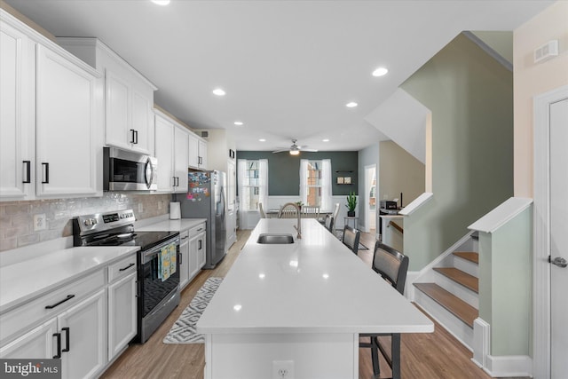 kitchen featuring a center island with sink, a sink, a kitchen breakfast bar, stainless steel appliances, and light wood-style floors