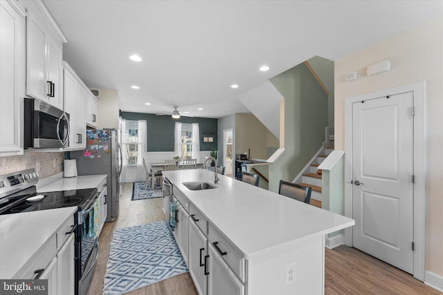 kitchen with light countertops, an island with sink, appliances with stainless steel finishes, white cabinets, and a sink