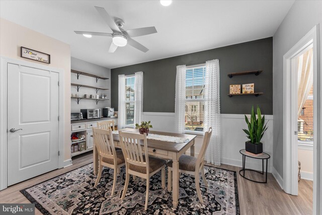 dining room featuring light wood-type flooring, a ceiling fan, and wainscoting