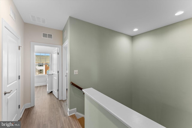 hallway with an upstairs landing, visible vents, light wood-style flooring, and recessed lighting