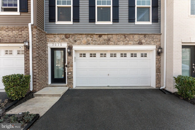 entrance to property featuring a garage, stone siding, brick siding, and driveway