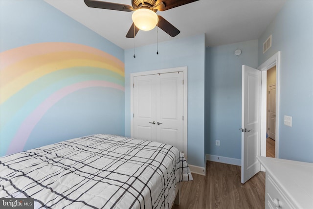 bedroom with a ceiling fan, visible vents, wood finished floors, baseboards, and a closet