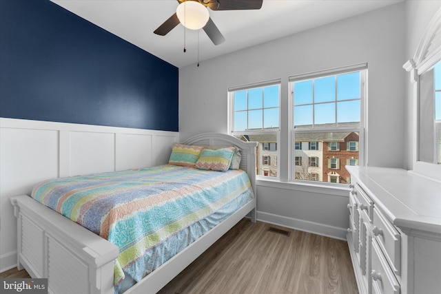 bedroom featuring visible vents, light wood-style floors, ceiling fan, and wainscoting