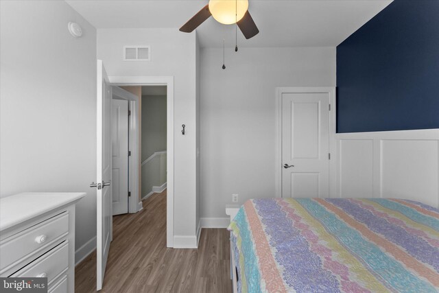 bedroom with visible vents, ceiling fan, a wainscoted wall, and wood finished floors