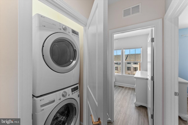 laundry area with visible vents, wood finished floors, stacked washing maching and dryer, baseboards, and laundry area