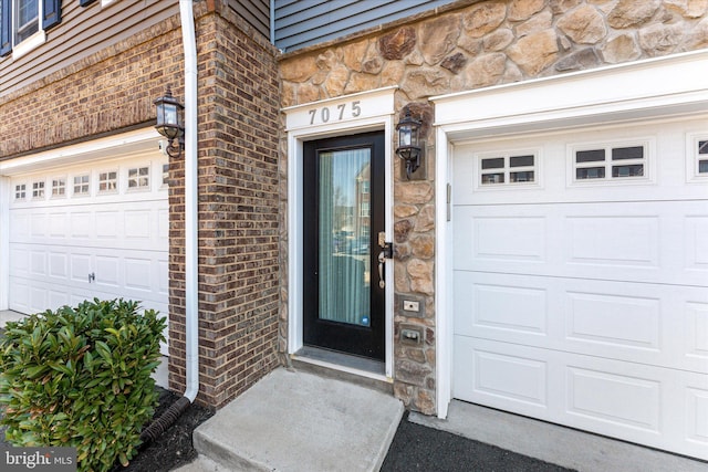 entrance to property with brick siding, stone siding, and a garage