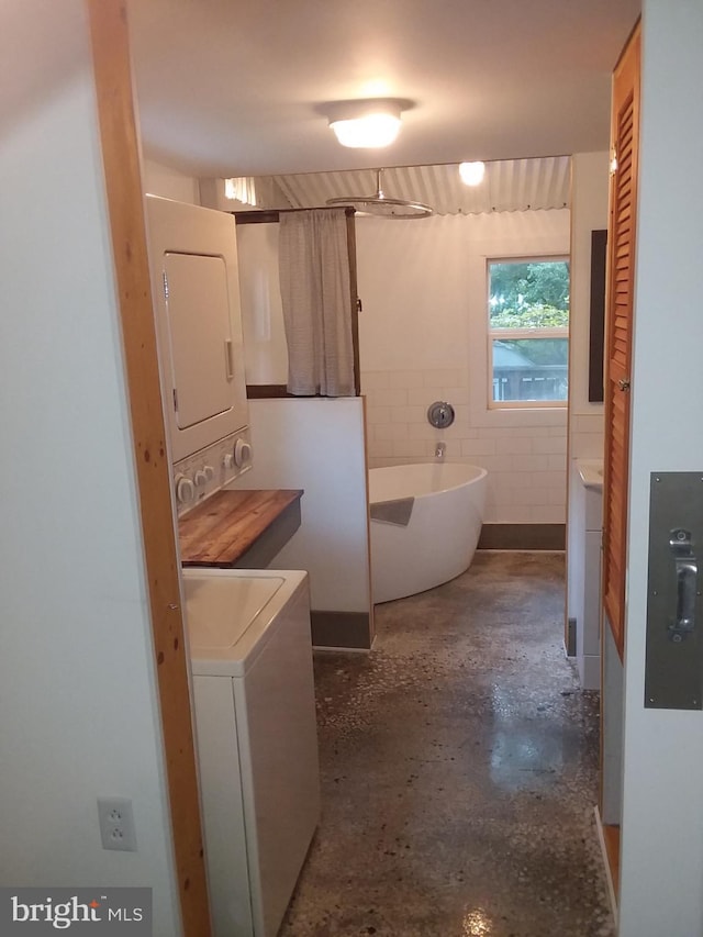 bathroom featuring a soaking tub, stacked washer and clothes dryer, and concrete flooring