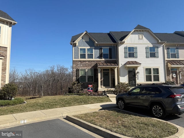 multi unit property featuring board and batten siding, a shingled roof, a front yard, stone siding, and uncovered parking