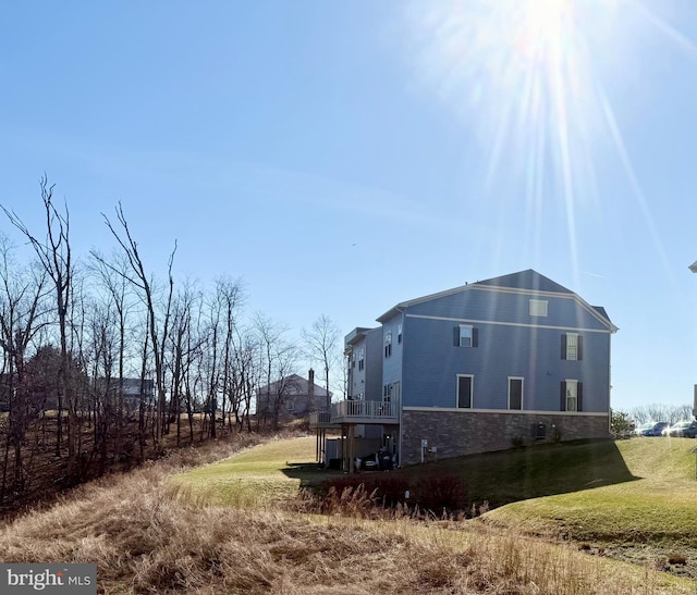 view of side of home with a yard, stone siding, and a wooden deck