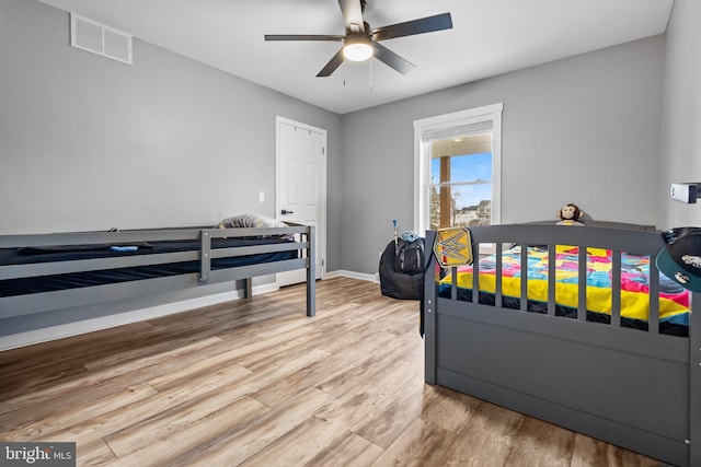 bedroom featuring a ceiling fan, visible vents, baseboards, and wood finished floors