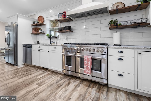 kitchen with extractor fan, appliances with stainless steel finishes, light stone countertops, open shelves, and light wood finished floors