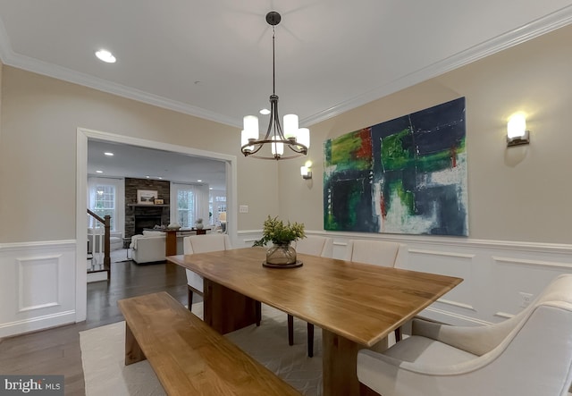 dining room with a wainscoted wall, a stone fireplace, crown molding, and wood finished floors