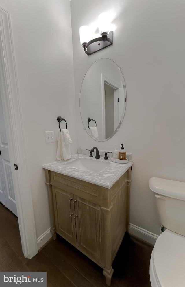 bathroom with vanity, toilet, wood finished floors, and baseboards