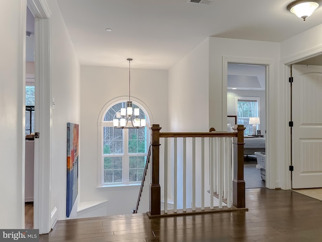 corridor with visible vents, an upstairs landing, a notable chandelier, and wood finished floors