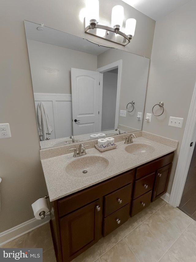 full bath with a sink, double vanity, tile patterned floors, and a decorative wall