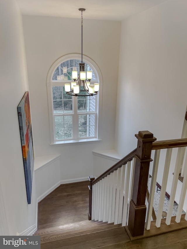 stairway with baseboards, an inviting chandelier, and wood finished floors