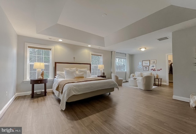 bedroom with visible vents, a raised ceiling, baseboards, and wood finished floors