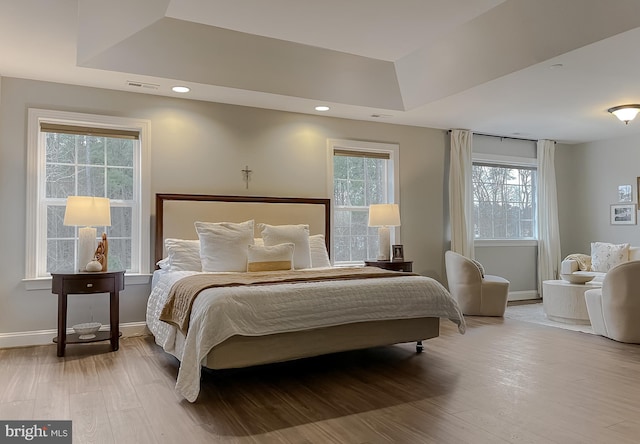 bedroom with a tray ceiling, wood finished floors, and visible vents