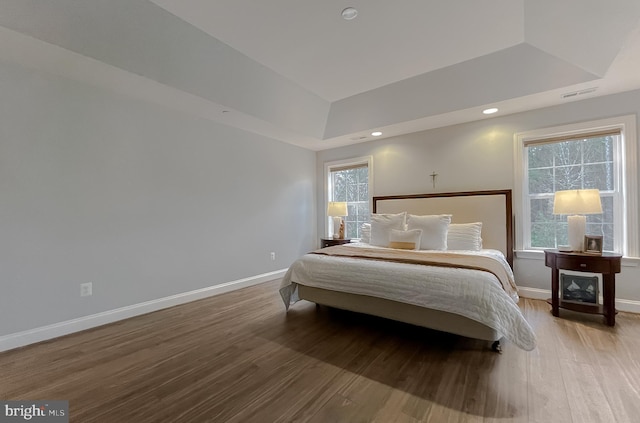 bedroom featuring a raised ceiling, wood finished floors, and baseboards