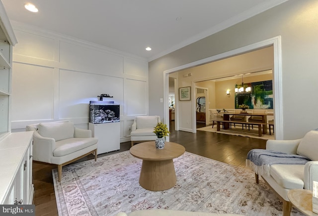 living area with an inviting chandelier, recessed lighting, ornamental molding, dark wood-type flooring, and a decorative wall