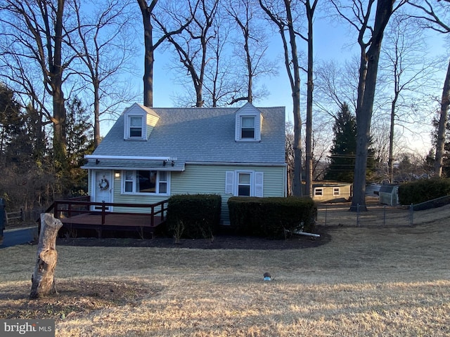 cape cod house with fence, roof with shingles, and a wooden deck